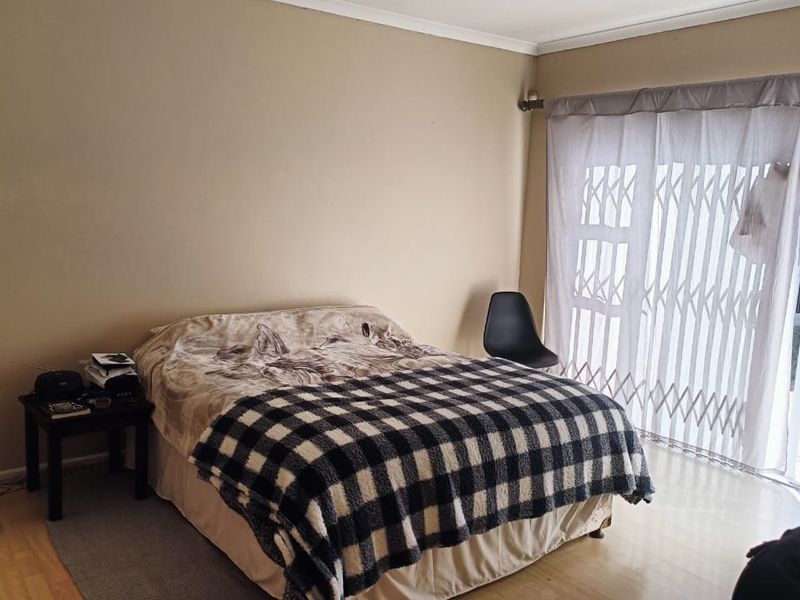 A bedroom featuring laminate flooring and a sliding glass door with an integrated security gate, providing direct access to the outdoor area.