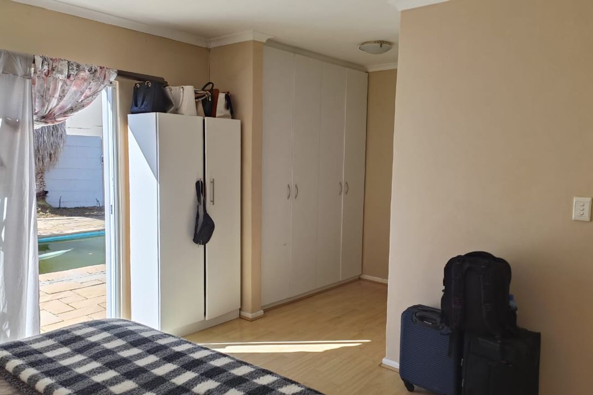 Bedroom featuring built-in cupboards, laminate flooring, and a sliding door providing direct access to the outdoor pool area.