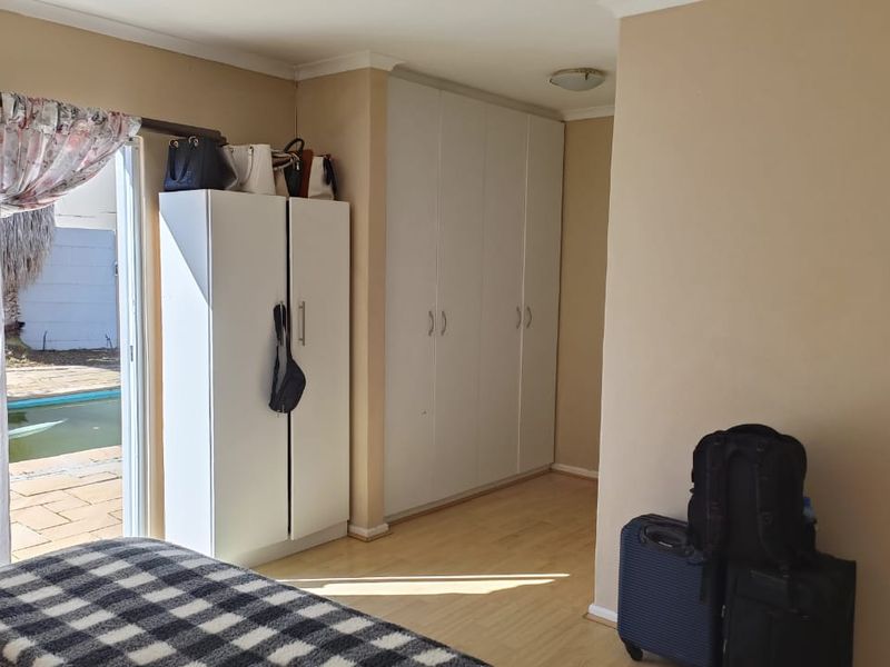 Bedroom featuring built-in cupboards, laminate flooring, and a sliding door providing direct access to the outdoor pool area.
