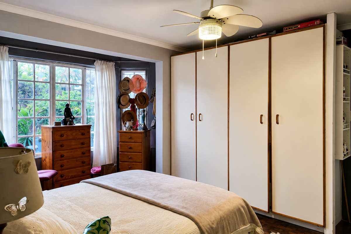 A bedroom featuring a large built-in wardrobe, ceiling fan, and parquet flooring, with a bay window providing natural light.