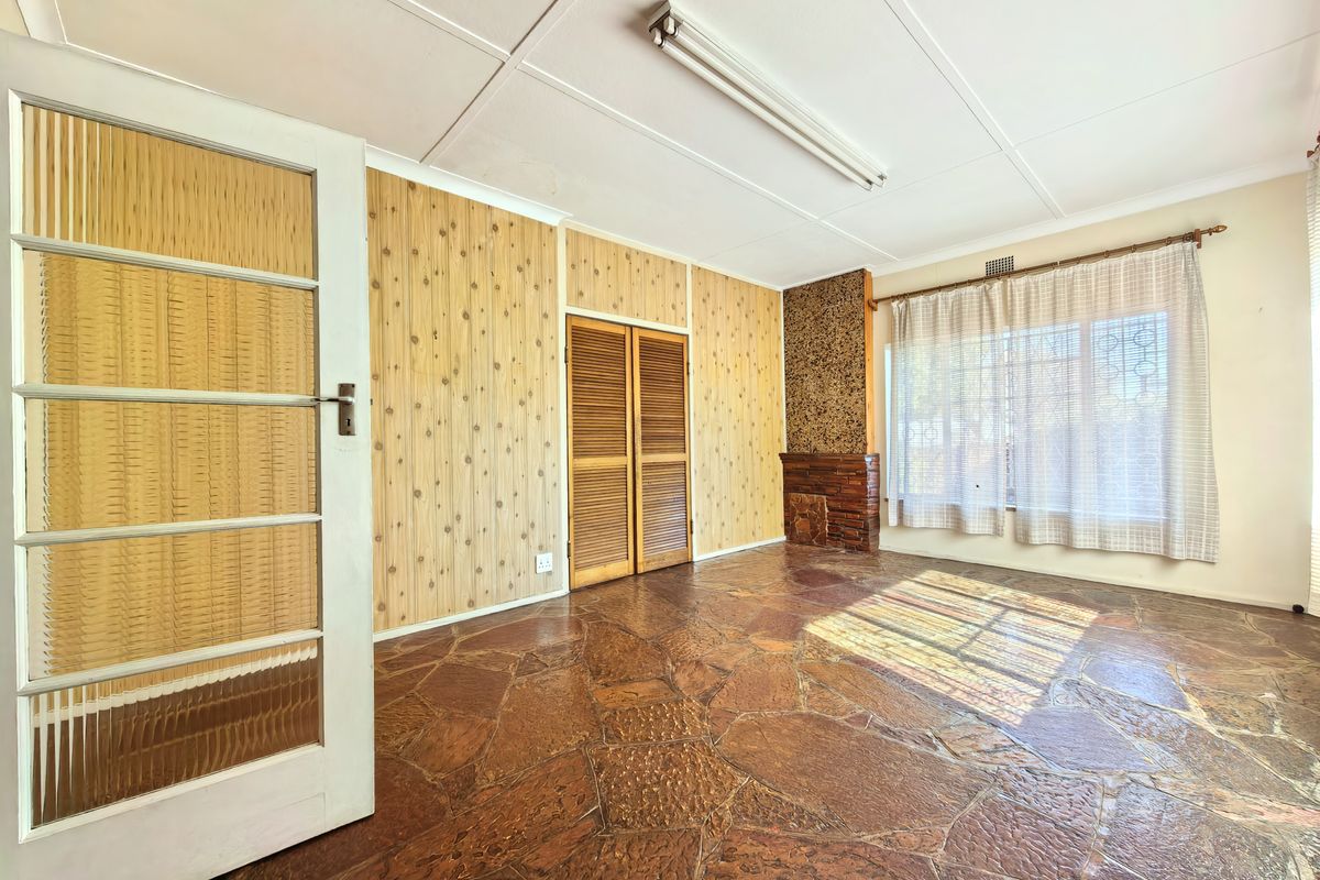 A spacious living room featuring unique flagstone flooring, wood-paneled walls, and a brick fireplace, offering a blank canvas for modernization.