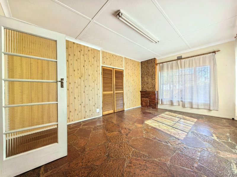 A spacious living room featuring unique flagstone flooring, wood-paneled walls, and a brick fireplace, offering a blank canvas for modernization.