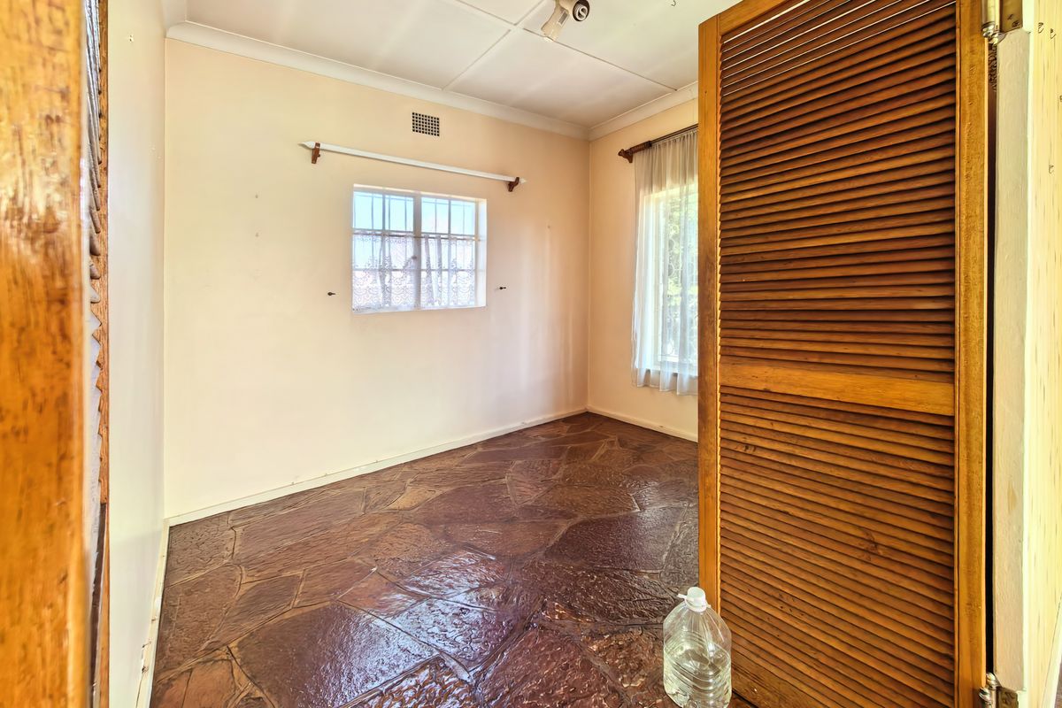 An empty bedroom featuring unique flagstone flooring, louvered timber closet doors, and security bars on the windows, offering a blank canvas for renovation.