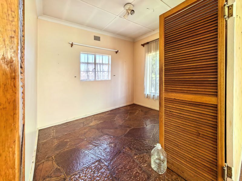 An empty bedroom featuring unique flagstone flooring, louvered timber closet doors, and security bars on the windows, offering a blank canvas for renovation.