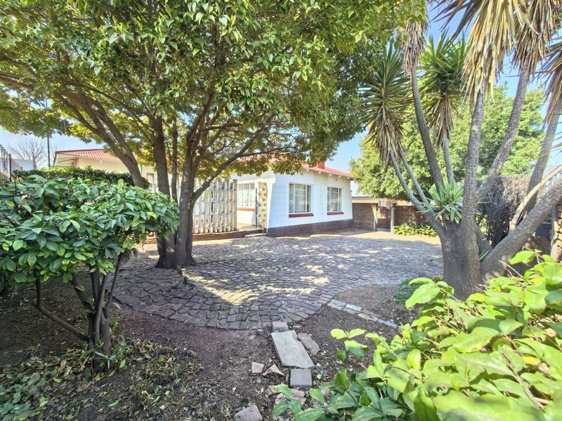 Front view of the property featuring a mature garden, established trees, and a circular cobblestone driveway leading to the main entrance.