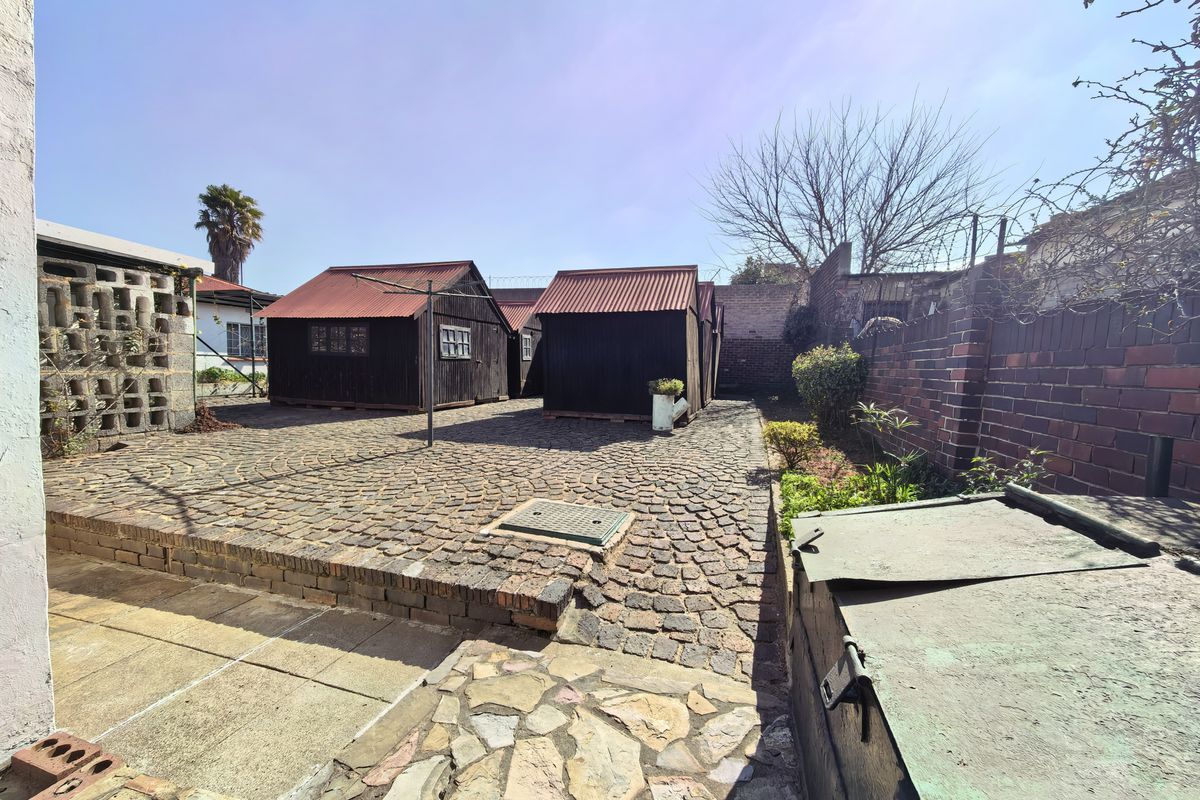 Rear courtyard area featuring cobblestone paving, brick boundary walls, and multiple detached timber outbuildings with metal roofing.