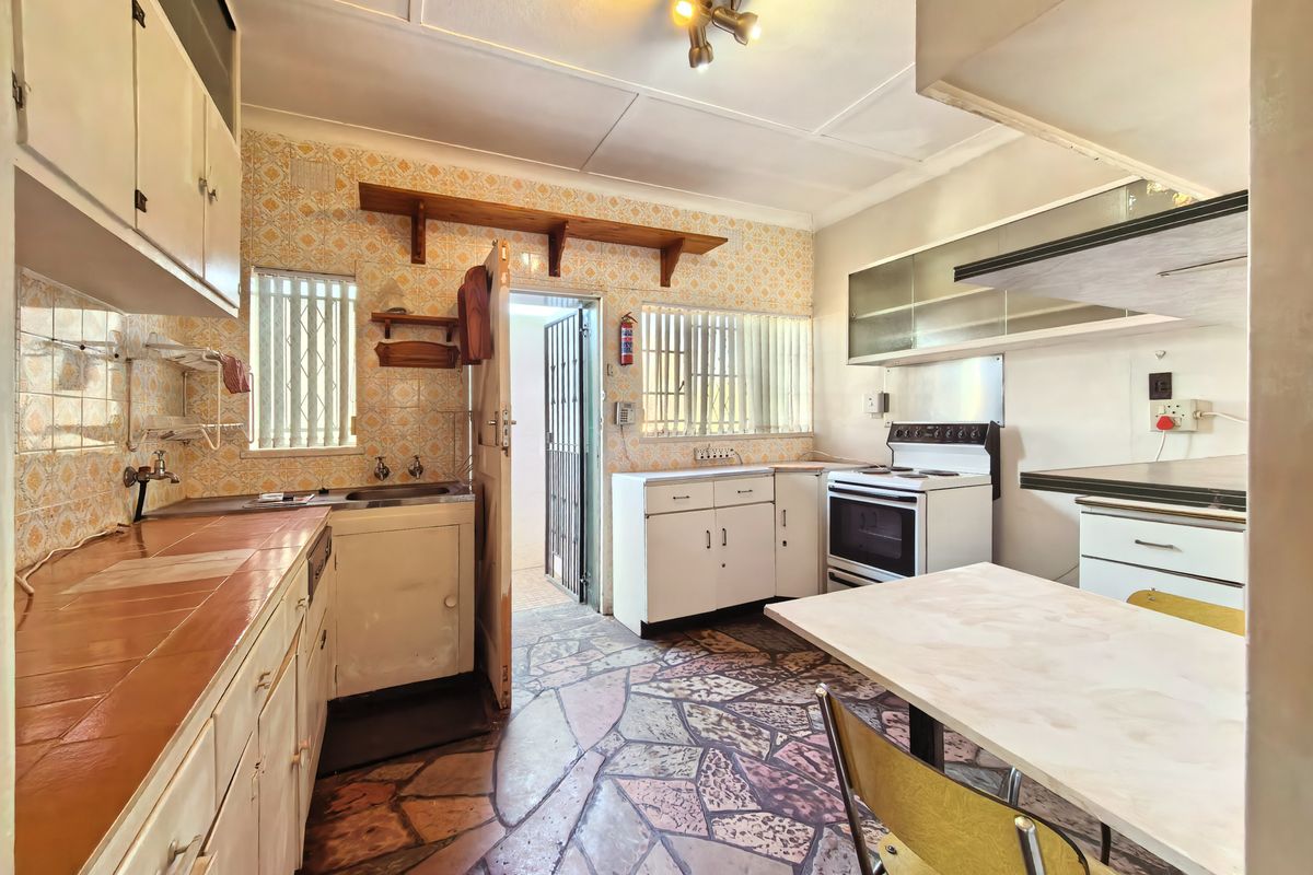 A dated kitchen featuring original cabinetry, tiled countertops, and stone flooring, offering significant potential for a modern renovation and layout update.