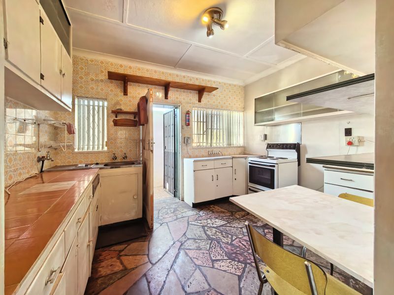 A dated kitchen featuring original cabinetry, tiled countertops, and stone flooring, offering significant potential for a modern renovation and layout update.