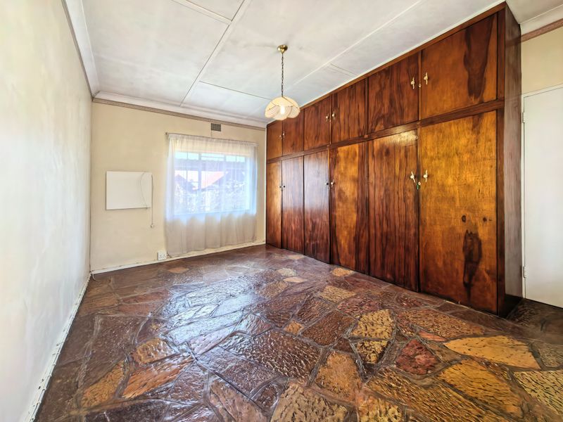 Empty bedroom featuring unique stone flooring, extensive built-in wooden cabinetry, and a classic pendant light fixture.