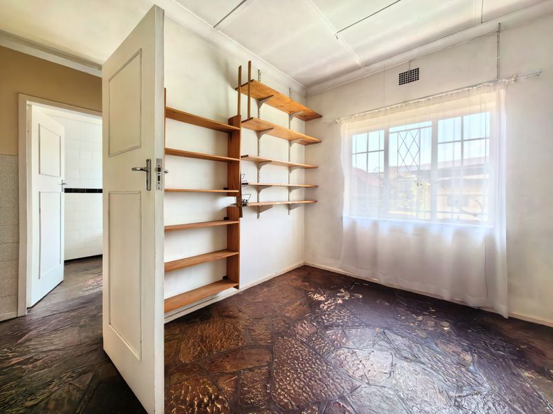 A vacant bedroom featuring unique stone flooring, built-in wall shelving, and a window with security bars, offering a blank canvas for renovation.