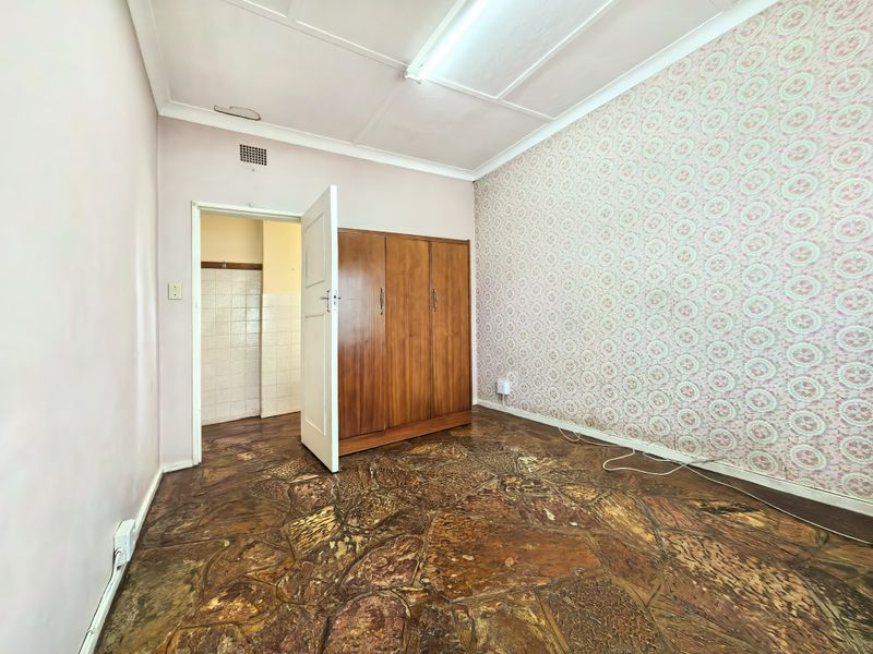 A bedroom featuring built-in cabinetry, patterned wallpaper, and stone-effect flooring, offering a blank canvas for renovation and modernization.