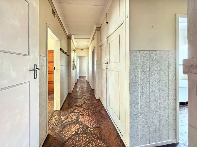 A long hallway featuring built-in storage cupboards, tiled wall wainscoting, and distinctive crazy paving stone flooring.