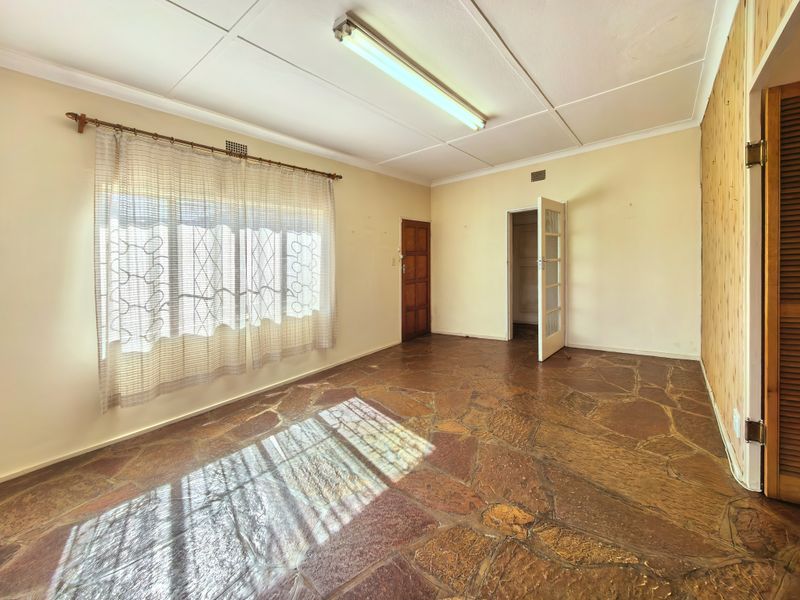 An empty living room featuring unique flagstone flooring, timber wall paneling, and dual access points through traditional timber and glass-paneled doors.