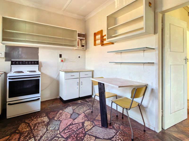 A compact, dated kitchen featuring original cabinetry, a freestanding stove, and distinctive stone-style flooring, offering significant potential for a modern renovation.
