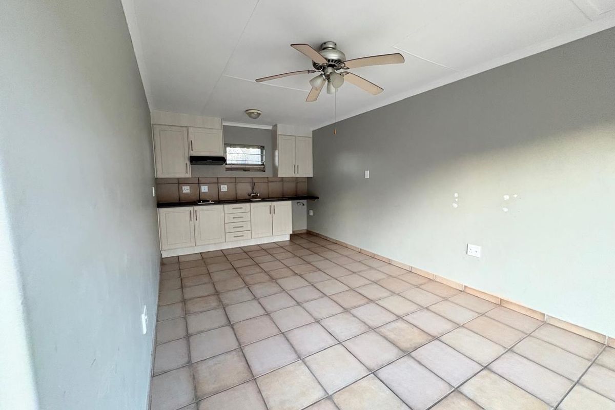 An open-plan kitchen and living area featuring tiled flooring, neutral cabinetry, and a ceiling fan, presenting a blank canvas for potential interior design updates.