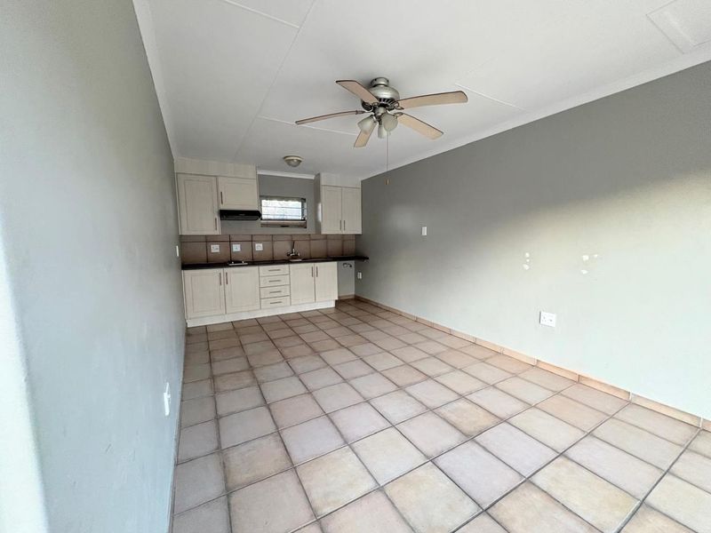 An open-plan kitchen and living area featuring tiled flooring, neutral cabinetry, and a ceiling fan, presenting a blank canvas for potential interior design updates.