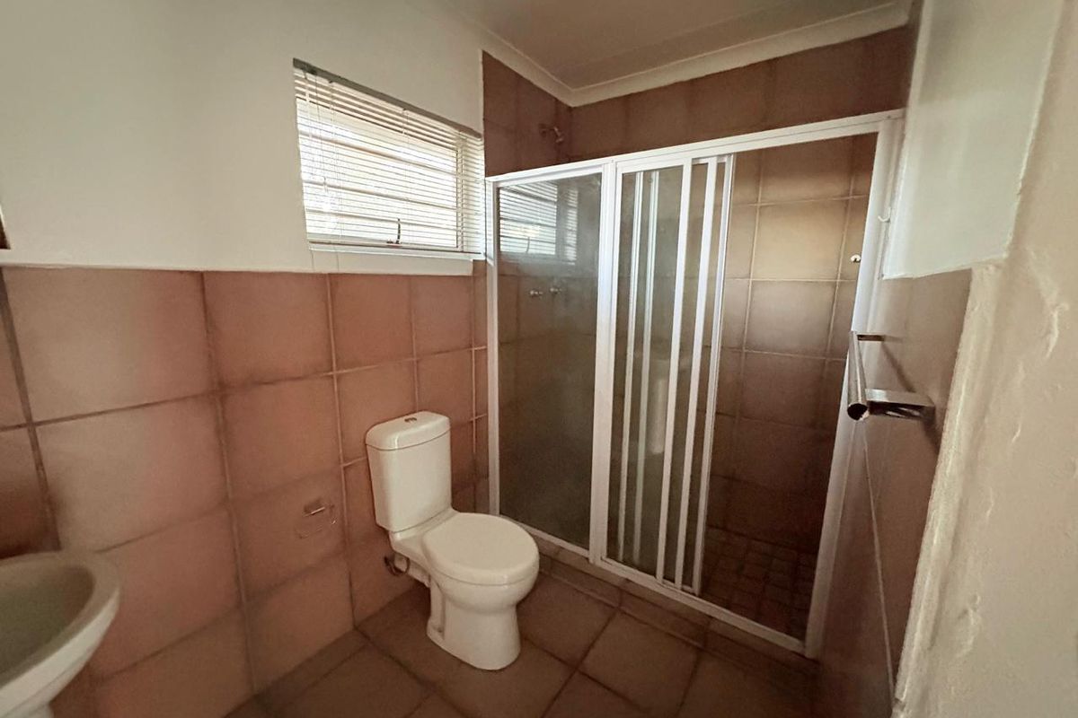 A functional bathroom featuring a shower enclosure, pedestal basin, and toilet, finished with neutral wall and floor tiling.