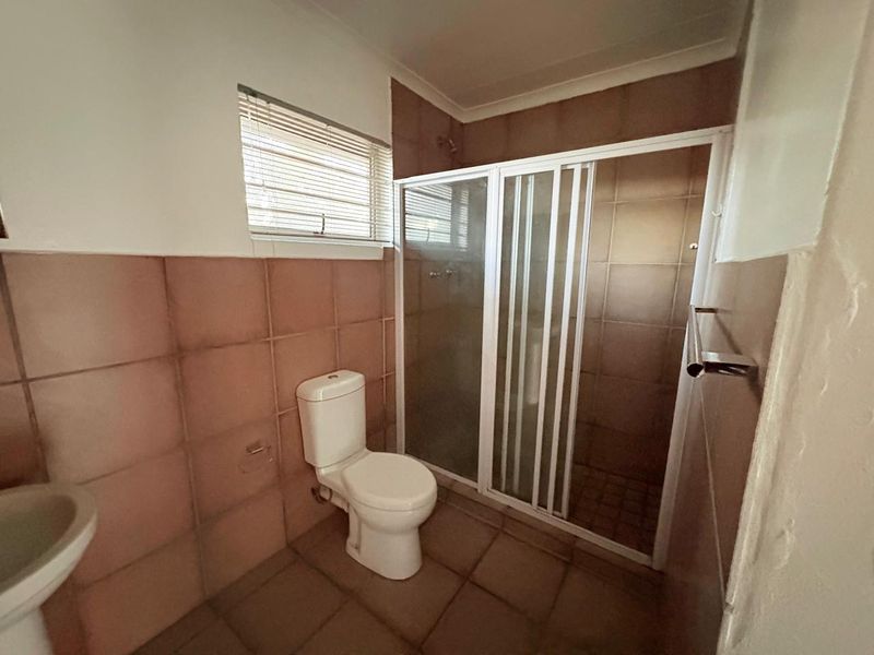 A functional bathroom featuring a shower enclosure, pedestal basin, and toilet, finished with neutral wall and floor tiling.