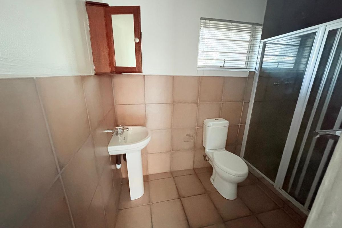 A functional bathroom featuring a pedestal basin, toilet, and shower enclosure with tiled finishes throughout.