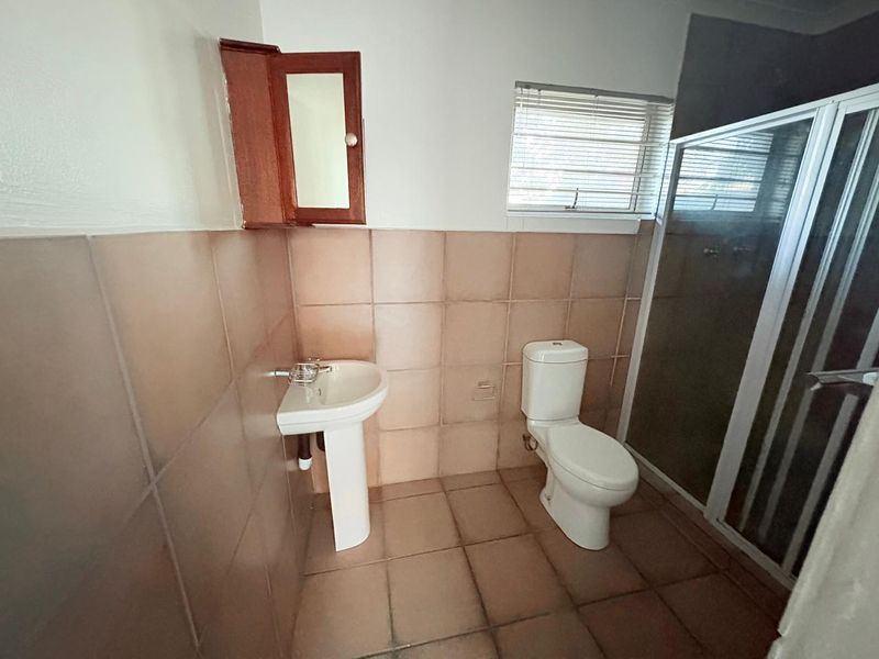 A functional bathroom featuring a pedestal basin, toilet, and shower enclosure with tiled finishes throughout.