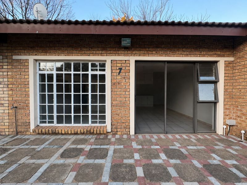 Rear exterior view of the flat featuring a brick facade, paved patio area, sliding glass door, and a grid-style window.