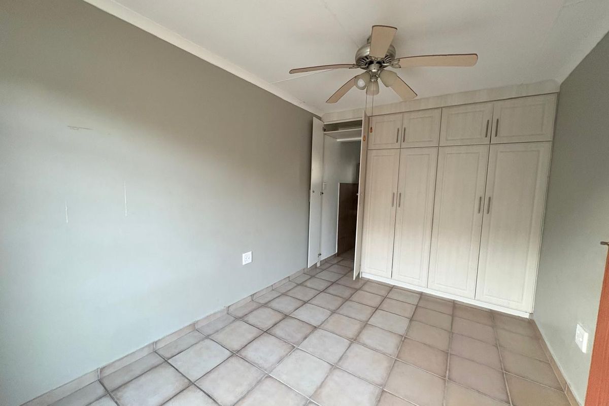 A spacious bedroom featuring neutral walls, tiled flooring, a ceiling fan, and ample built-in cupboard storage.