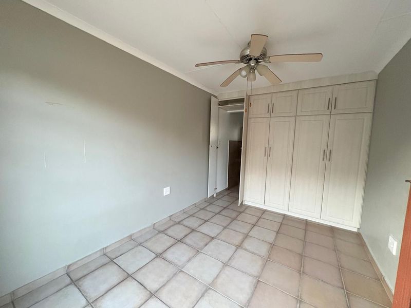 A spacious bedroom featuring neutral walls, tiled flooring, a ceiling fan, and ample built-in cupboard storage.