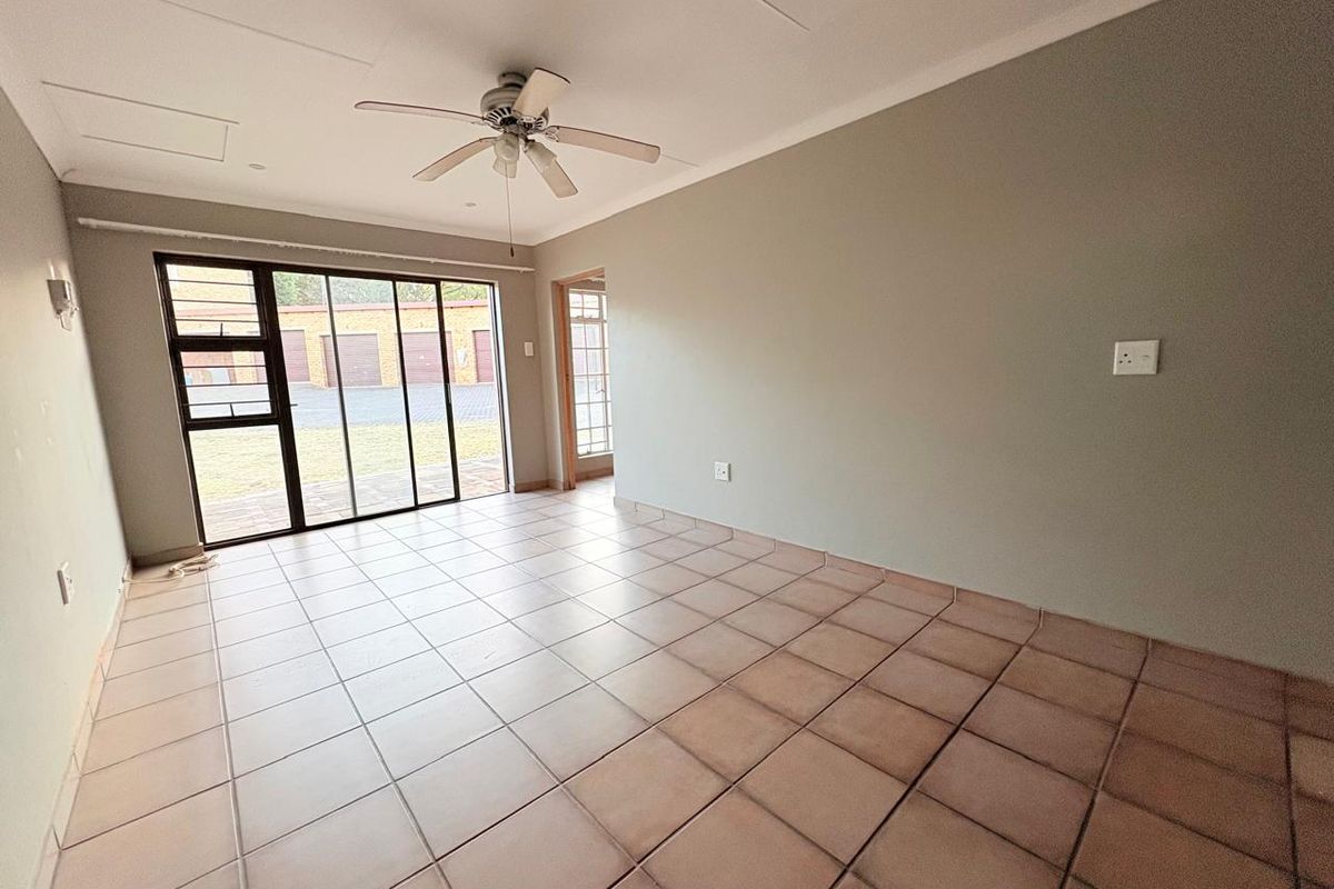 A spacious, empty living area featuring neutral walls, tiled flooring, a ceiling fan, and large sliding glass doors providing natural light and outdoor access.