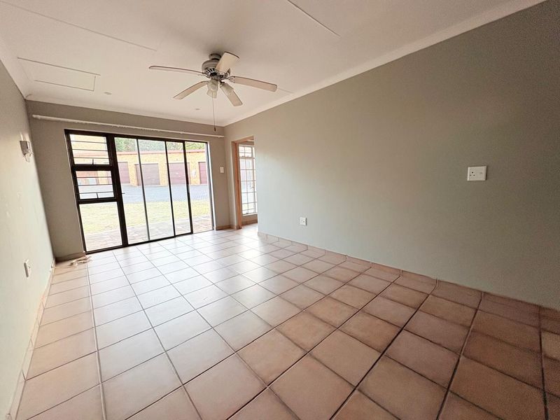 A spacious, empty living area featuring neutral walls, tiled flooring, a ceiling fan, and large sliding glass doors providing natural light and outdoor access.