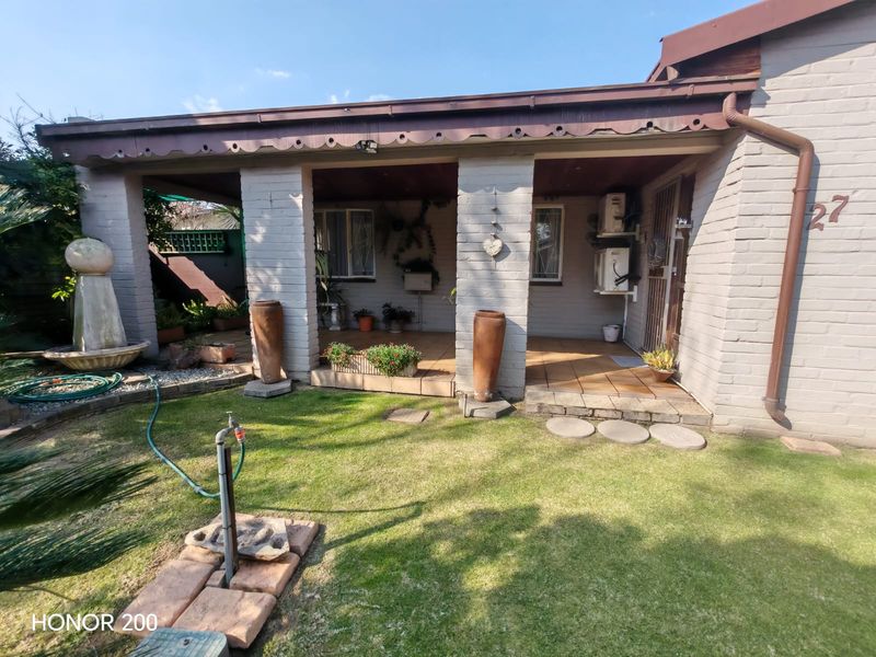 A covered rear patio area featuring brick pillars, tiled flooring, and external air conditioning units, overlooking a small garden space.