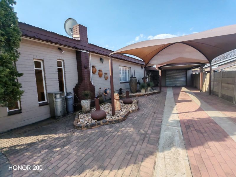Front exterior view featuring a paved driveway, a shade sail carport, and a brick facade with a chimney.