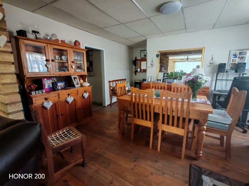 A dining room featuring timber flooring, an exposed brick fireplace, and a drop ceiling, offering a traditional layout with potential for modernization.