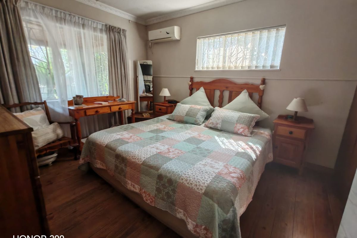 A cozy bedroom featuring warm timber flooring, ceiling cornice detailing, and a wall-mounted air conditioning unit.