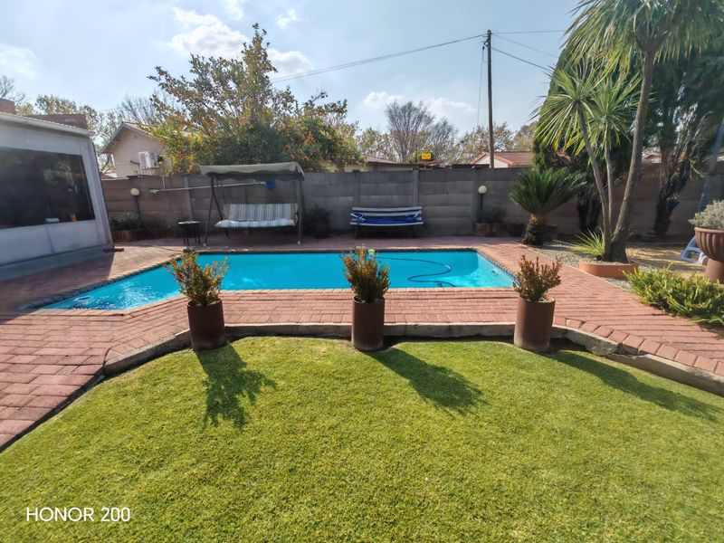 A well-maintained outdoor pool area featuring a clear swimming pool, brick paved surround, and a manicured lawn.