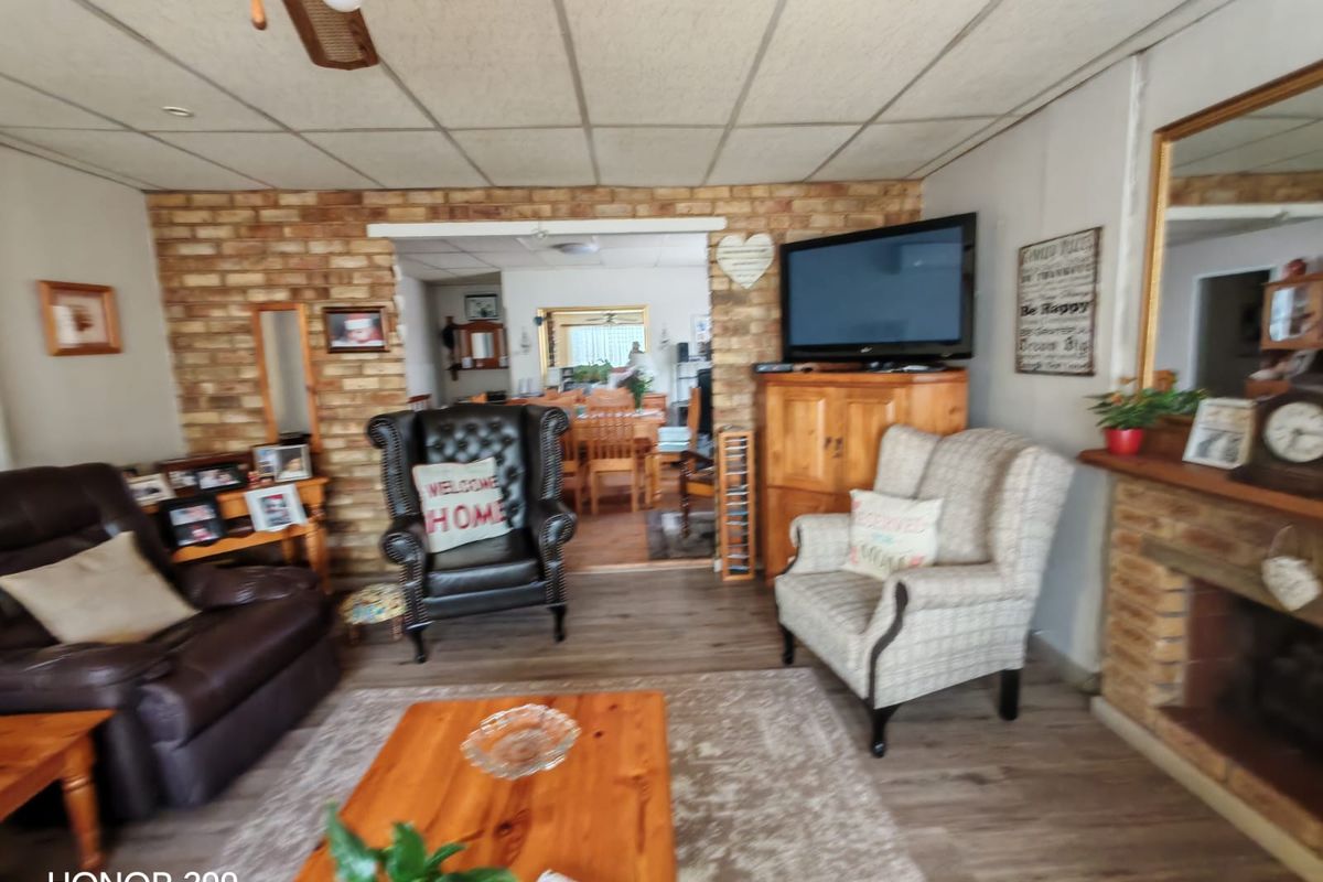 A living room featuring an exposed brick wall, fireplace, and ceiling fan, with an open-plan layout leading to the dining area.