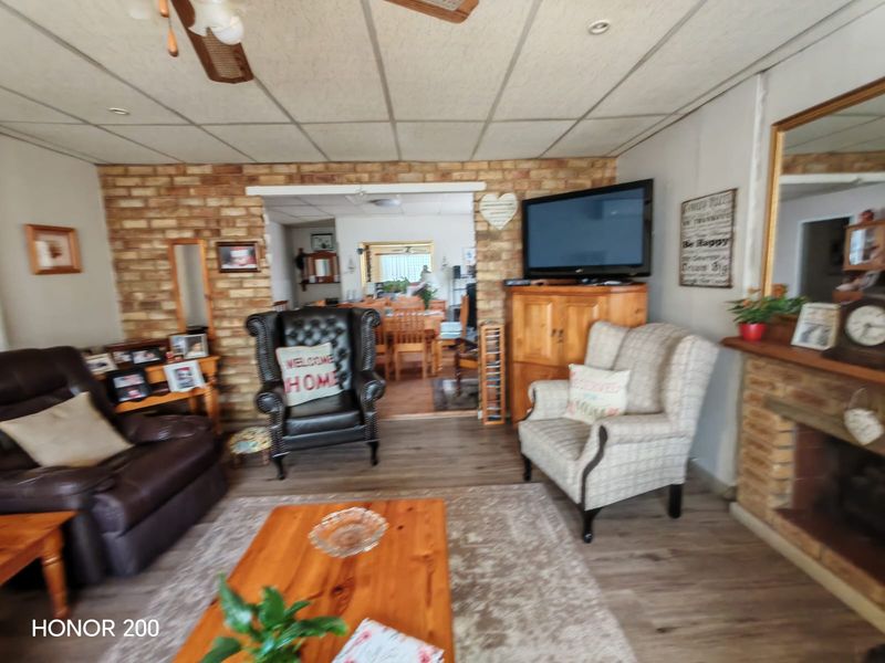 A living room featuring an exposed brick wall, fireplace, and ceiling fan, with an open-plan layout leading to the dining area.