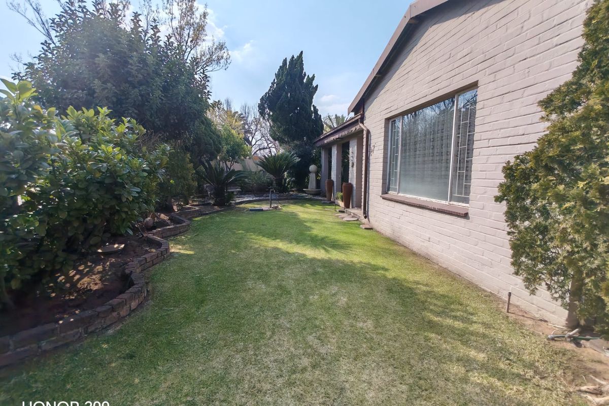 A well-maintained rear garden featuring a manicured lawn, established shrubbery, brick garden borders, and a view of the property's brick exterior wall.