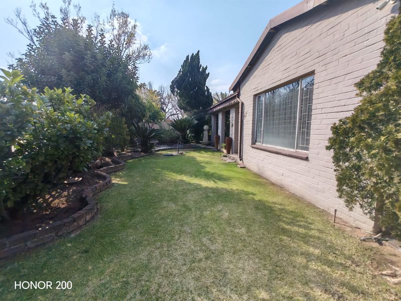 A well-maintained rear garden featuring a manicured lawn, established shrubbery, brick garden borders, and a view of the property's brick exterior wall.