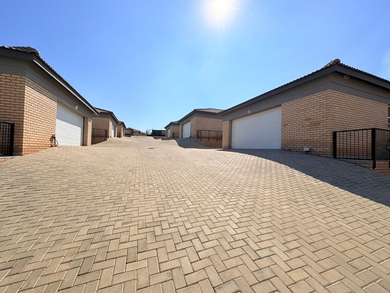 A view of the townhouse complex driveway featuring paved surfaces, brick facades, and multiple sectional garage doors under a clear sky.