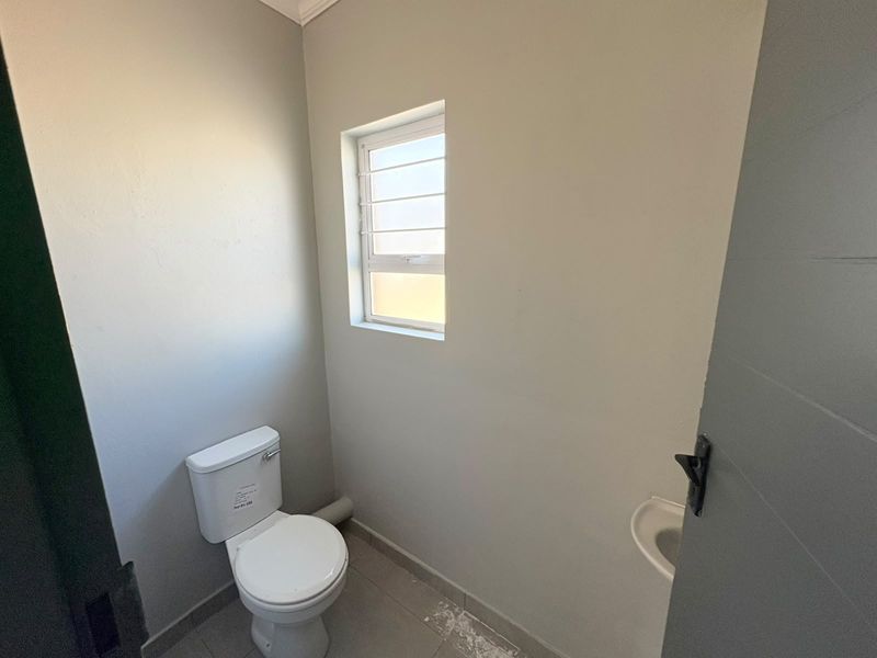 A compact guest bathroom featuring a toilet, wall-mounted basin, and tiled flooring, presenting a clean and functional space.