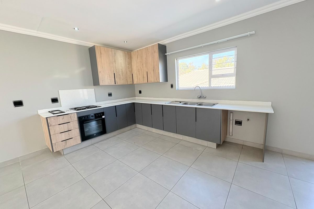 Modern kitchen featuring two-tone cabinetry, stone countertops, built-in oven, gas hob, and tiled flooring in a clean, open-plan layout.