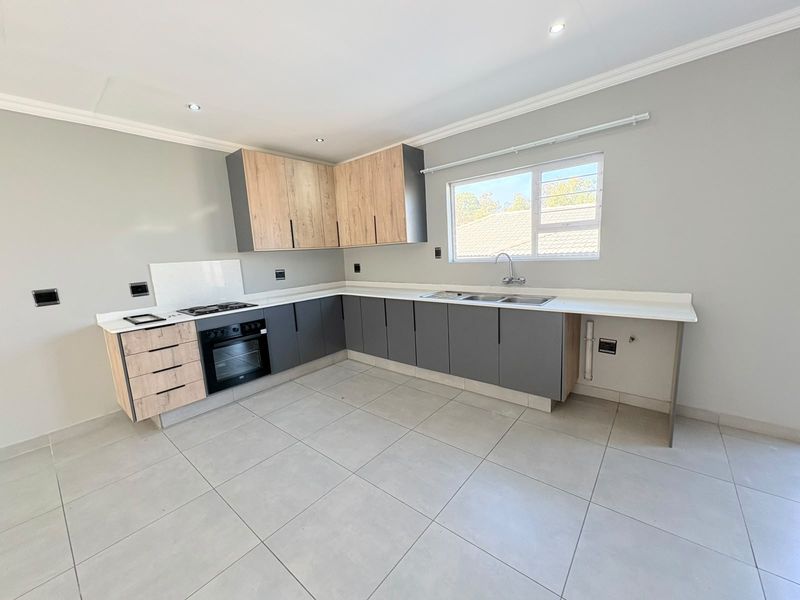 Modern kitchen featuring two-tone cabinetry, stone countertops, built-in oven, gas hob, and tiled flooring in a clean, open-plan layout.