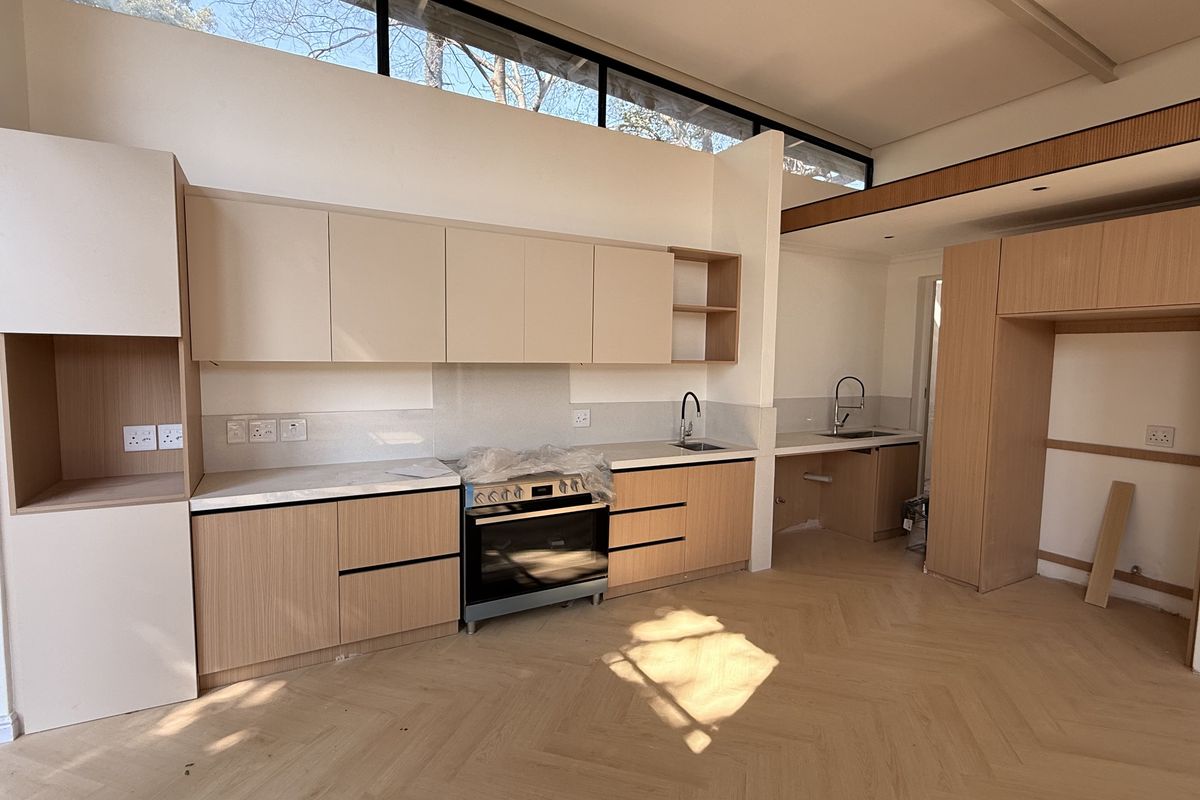 Modern kitchen featuring light wood cabinetry, stone countertops, herringbone flooring, and clerestory windows, currently in the final stages of installation.