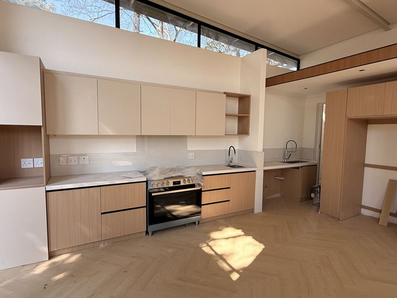Modern kitchen featuring light wood cabinetry, stone countertops, herringbone flooring, and clerestory windows, currently in the final stages of installation.