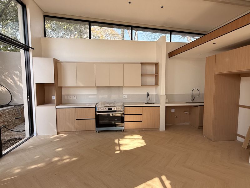Modern, light-filled kitchen featuring sleek cabinetry, herringbone timber flooring, and large glass doors opening to an outdoor area.