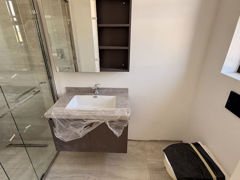 Modern bathroom featuring a glass shower enclosure, wall-mounted vanity with integrated basin, and a wall-mounted toilet. The space is newly finished and clean.