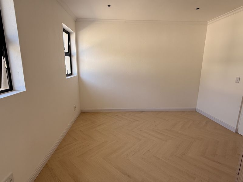 A bright, empty bedroom featuring modern herringbone flooring, built-in wardrobes, and recessed downlights, offering a clean and neutral space ready for personalization.