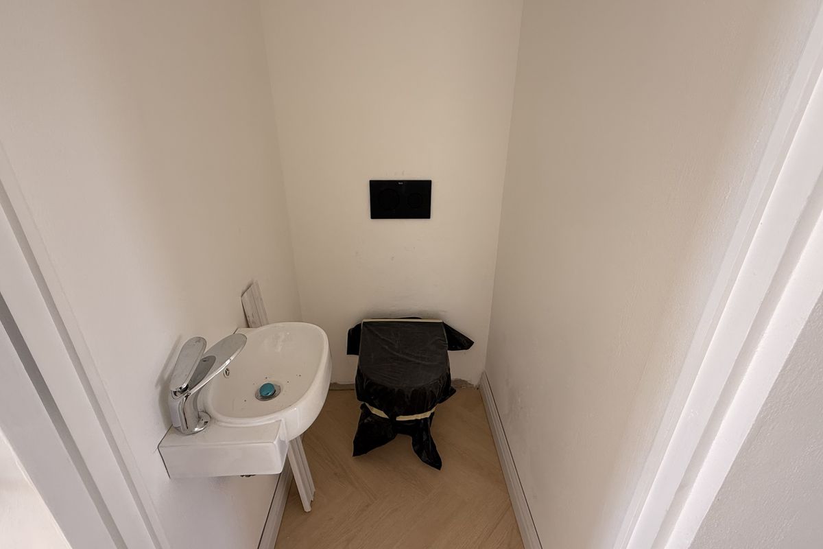 A small guest bathroom or powder room featuring a wall-mounted basin and concealed cistern, currently undergoing final finishing touches.