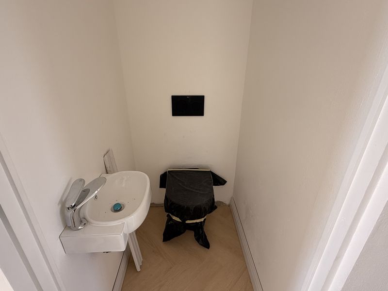 A small guest bathroom or powder room featuring a wall-mounted basin and concealed cistern, currently undergoing final finishing touches.