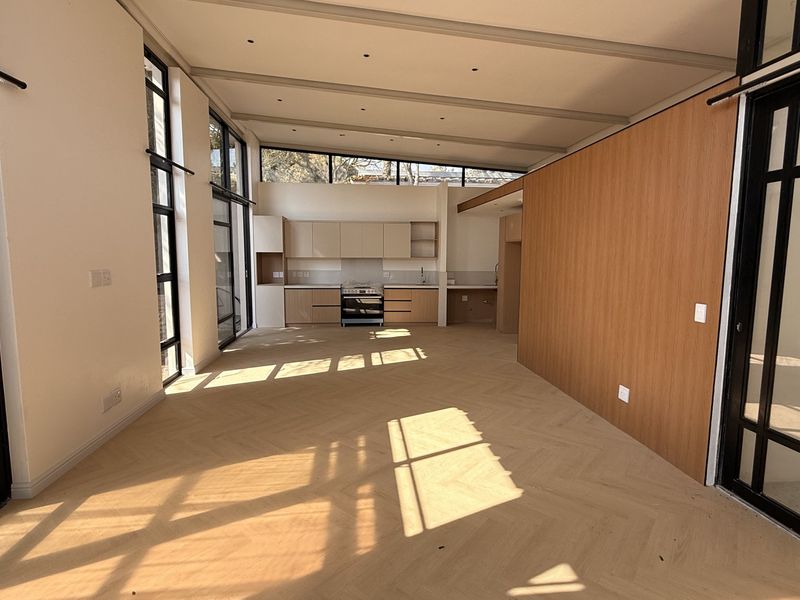 Spacious open-plan living and kitchen area featuring modern herringbone timber flooring, sleek cabinetry, and expansive black steel-framed glass doors providing abundant natural light.